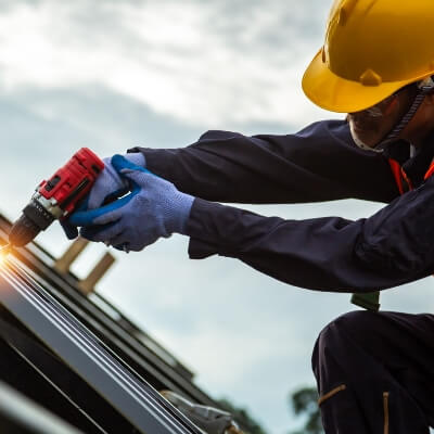 Solar panel technician with drill installing solar panels on roof